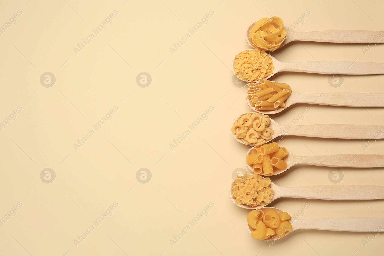 Photo of Different types of pasta in spoons on beige background, flat lay. Space for text