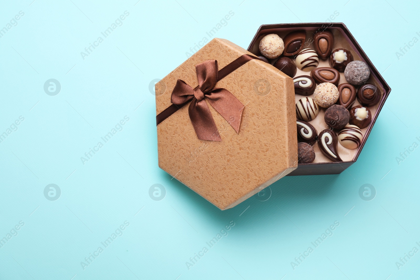 Photo of Box of delicious chocolate candies on light blue background, top view. Space for text