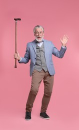 Senior man with walking cane winking on pink background
