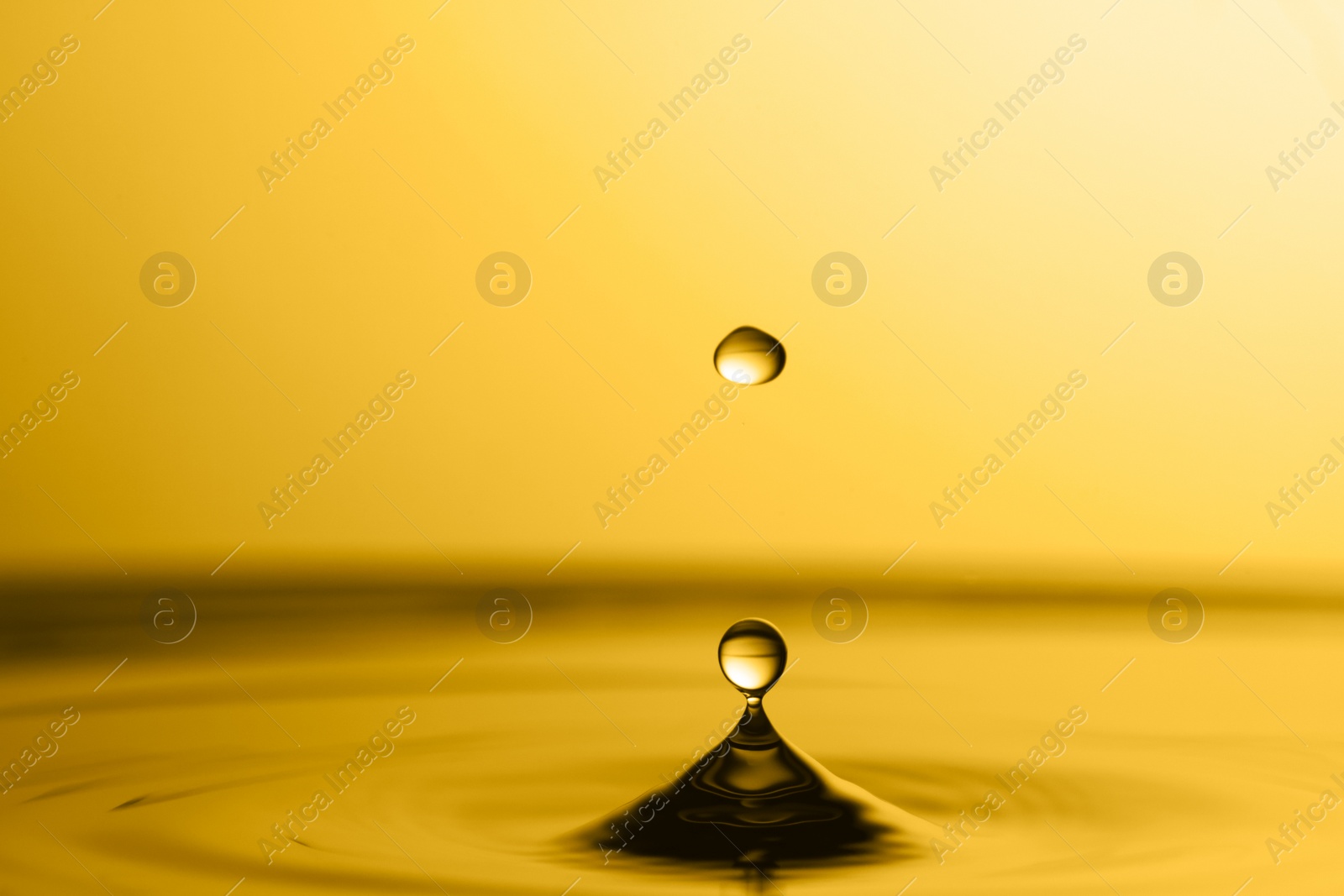 Image of Splash of golden oily liquid with drop on yellow background, closeup. Space for text