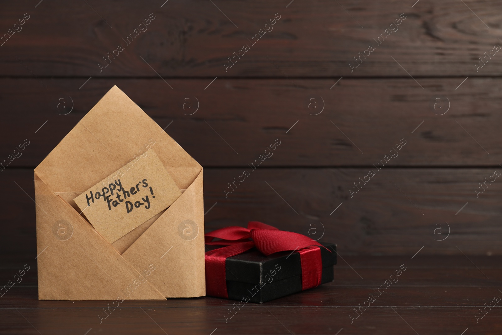 Photo of Card with phrase Happy Father's Day in envelope and gift box on wooden table, closeup. Space for text
