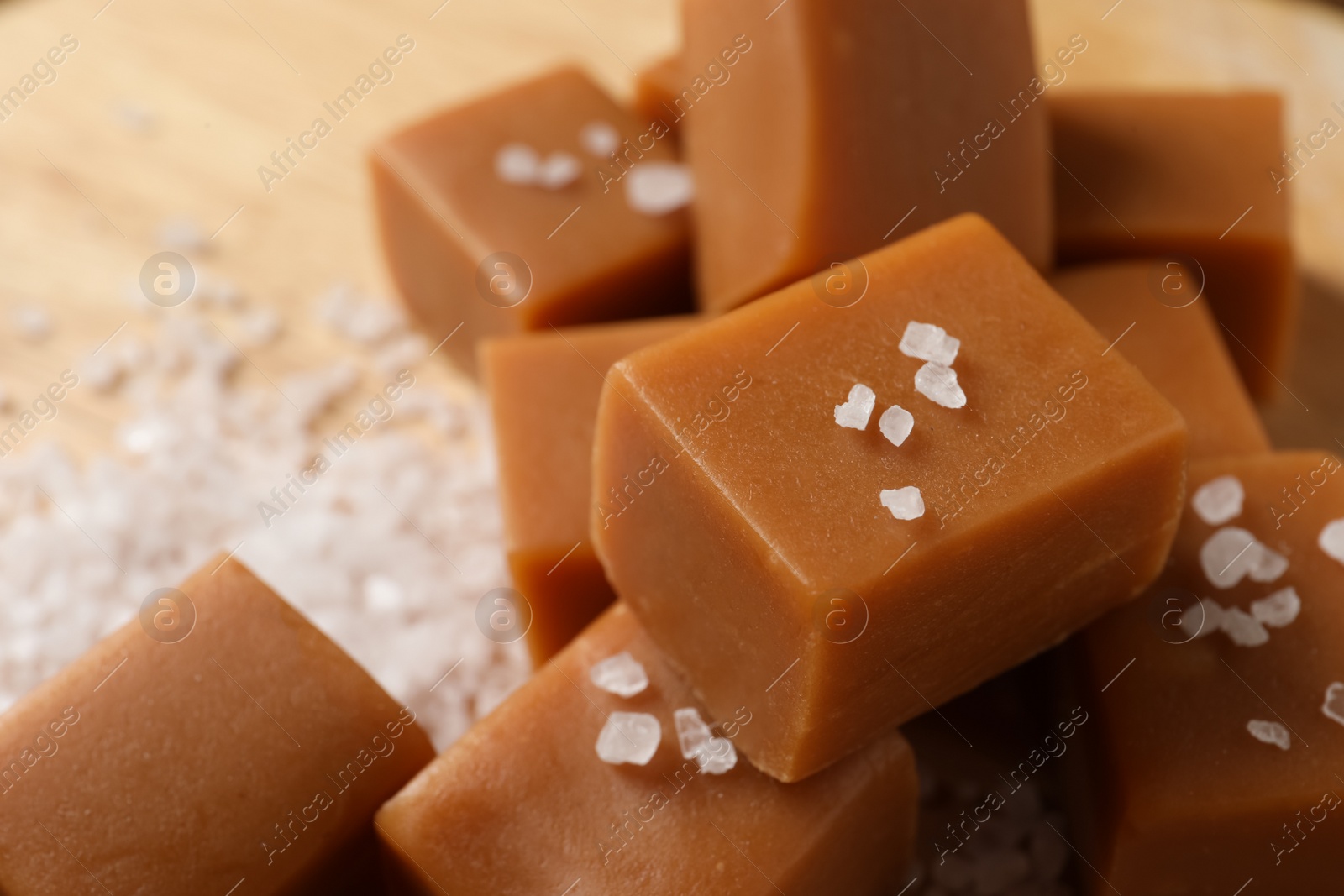 Photo of Yummy caramel candies and sea salt on table, closeup