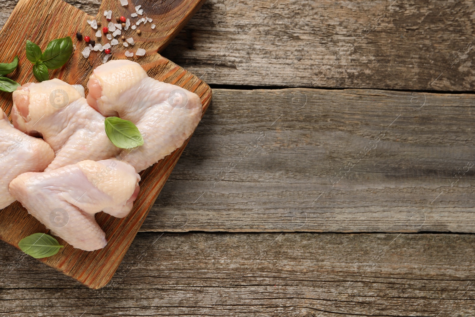 Photo of Raw chicken wings with basil and spices on wooden table, top view. Space for text