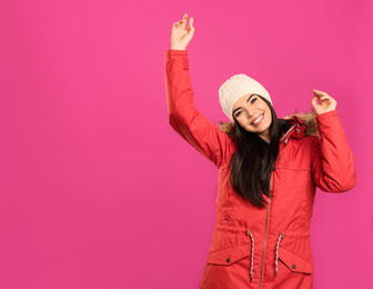 Photo of Happy young woman in warm clothes on pink background, space for text. Winter vacation