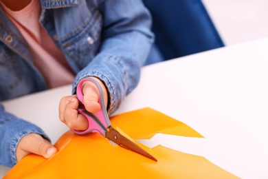 Photo of Little girl left-handed cutting construction paper at table, closeup