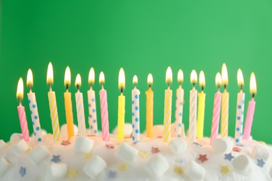 Photo of Birthday cake with burning candles on green background, closeup