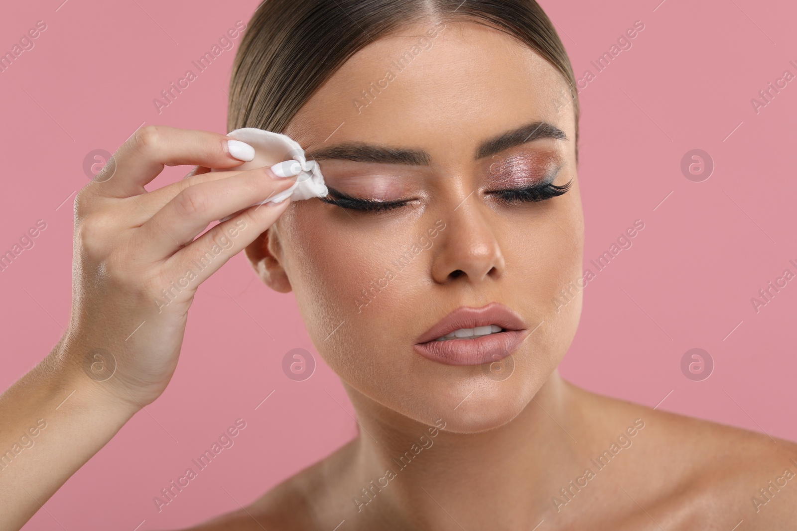 Photo of Beautiful woman removing makeup with cotton pad on pink background, closeup