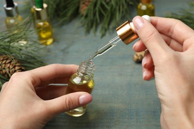 Woman holding bottle with pine essential oil at light blue wooden table, closeup