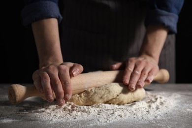 Photo of Making bread. Woman rolling dough at table on dark background, closeup