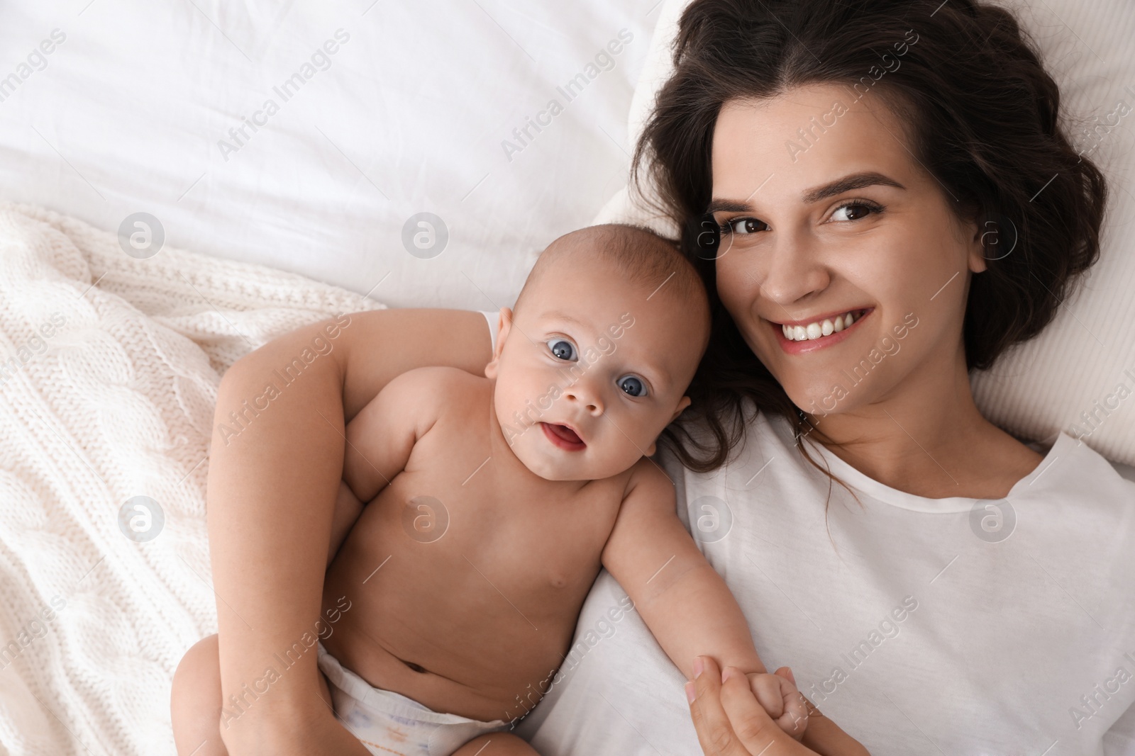 Photo of Happy young mother with her cute baby on bed, top view