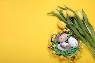 Flat lay composition with beautiful flowers and eggs on yellow background, space for text. Easter celebration