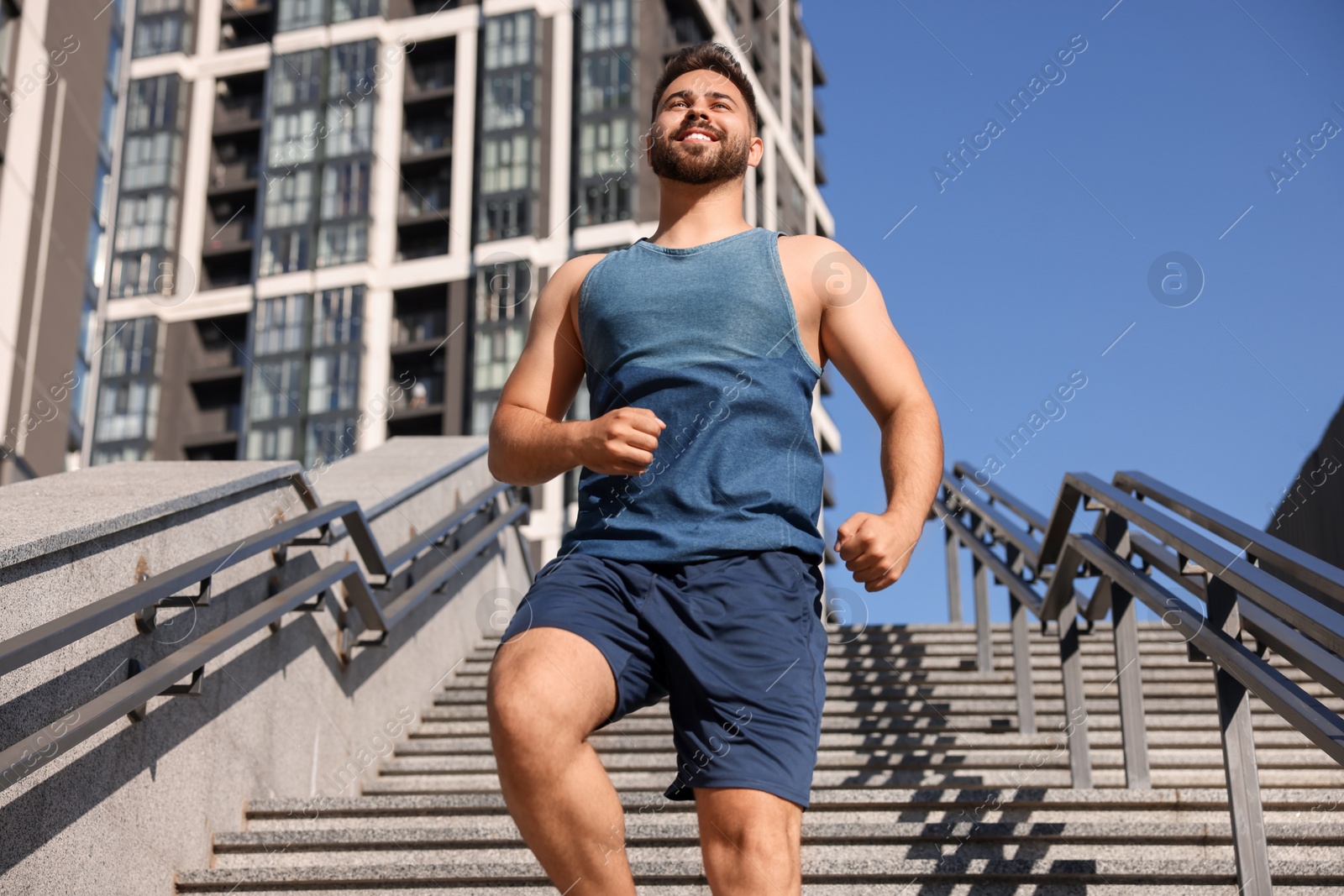 Photo of Happy man running down stairs outdoors on sunny day, low angle view