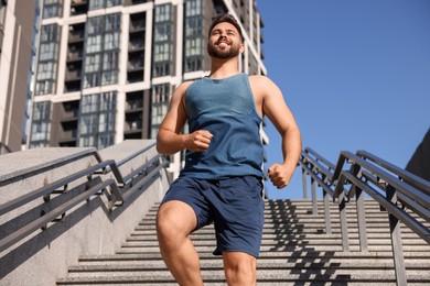 Photo of Happy man running down stairs outdoors on sunny day, low angle view