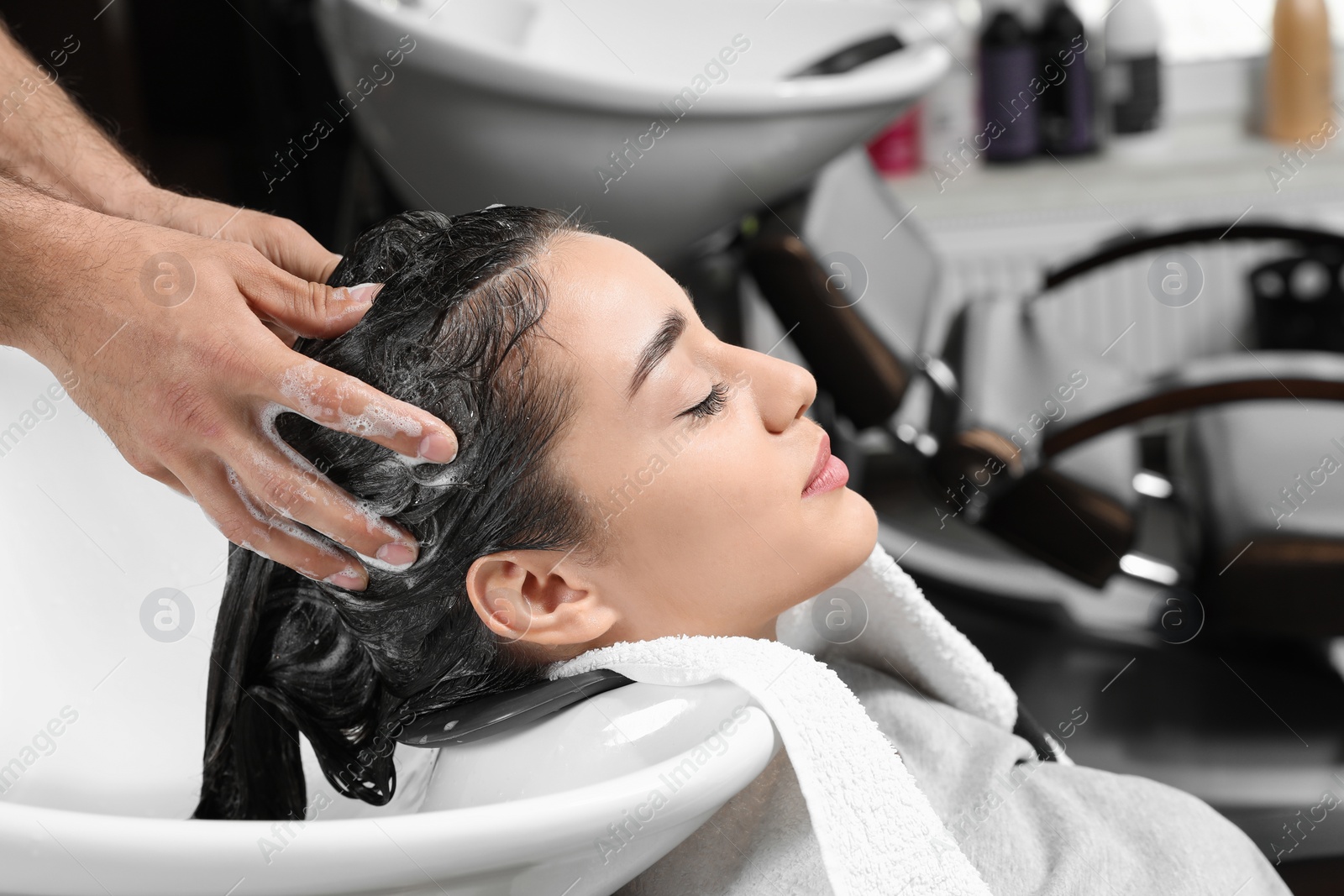 Photo of Stylist washing client's hair at sink in beauty salon