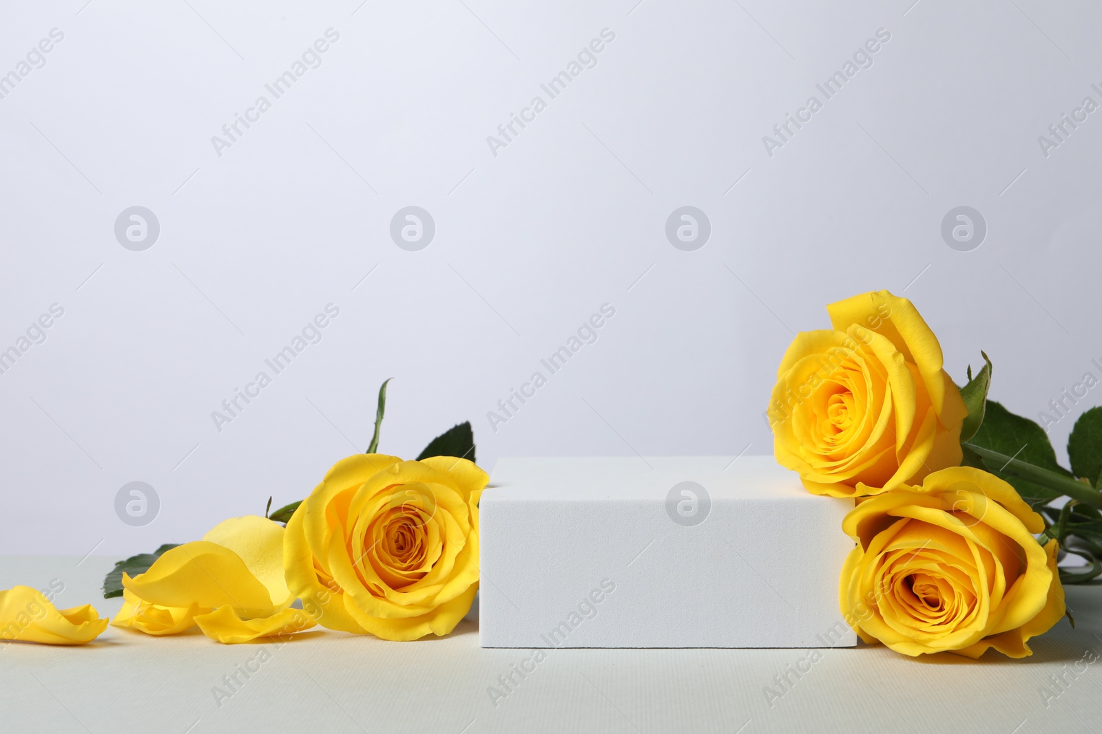 Photo of Beautiful presentation for product. Square podium and yellow roses on white table, space for text
