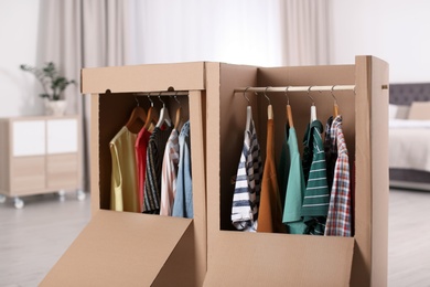 Photo of Cardboard wardrobe boxes with clothes on hangers in bedroom