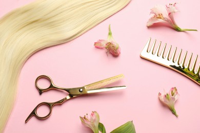 Photo of Hairdresser tools. Blonde hair lock, comb, scissors and flowers on pink background, flat lay