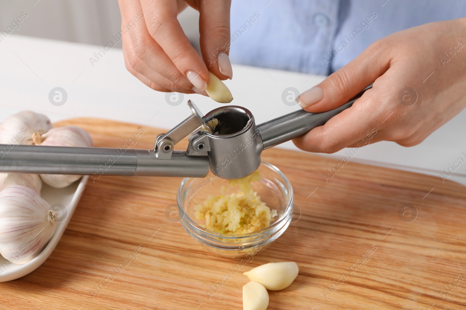 Photo of Woman squeezing garlic with press at wooden table, closeup