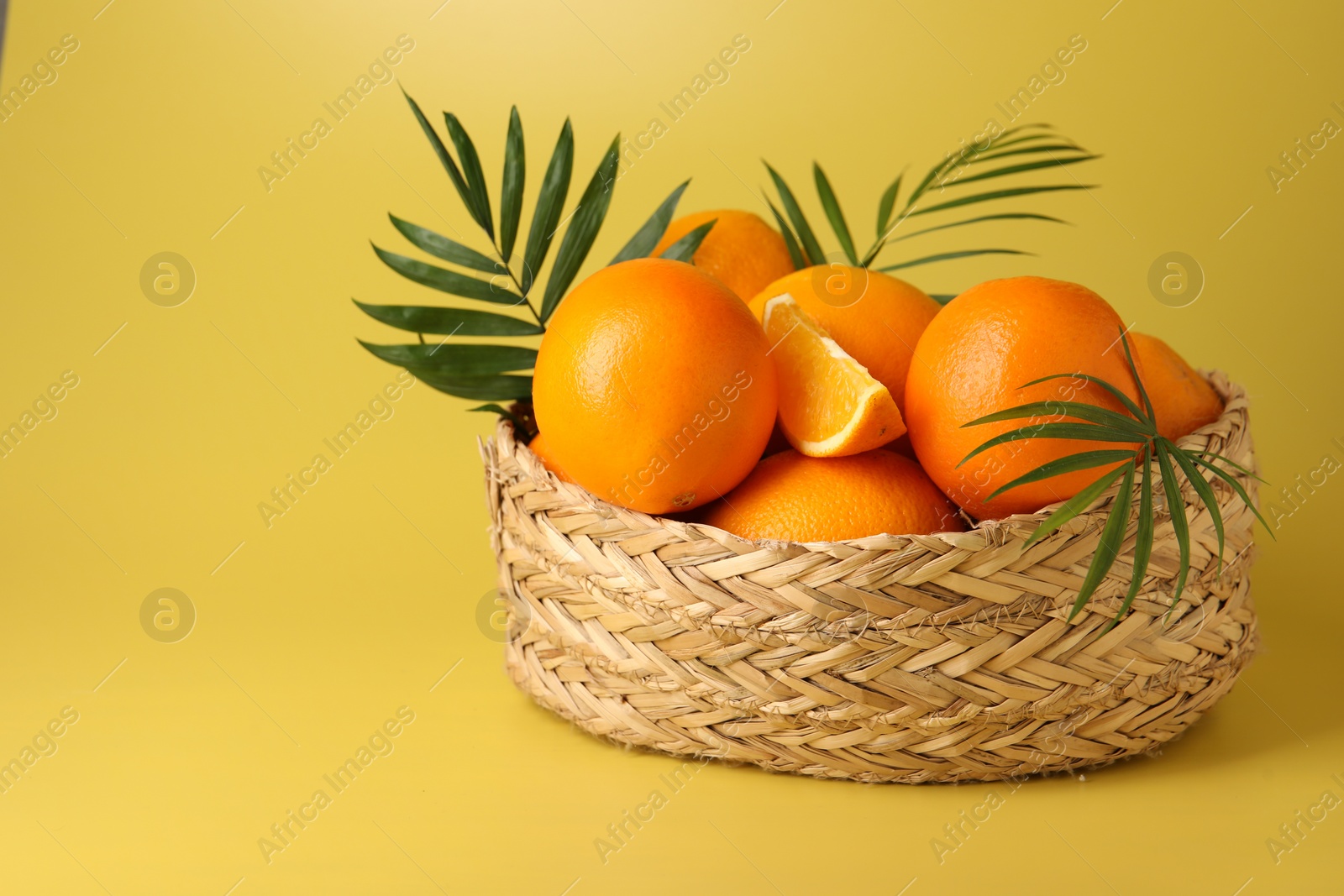 Photo of Fresh oranges in wicker basket on yellow background. Space for text