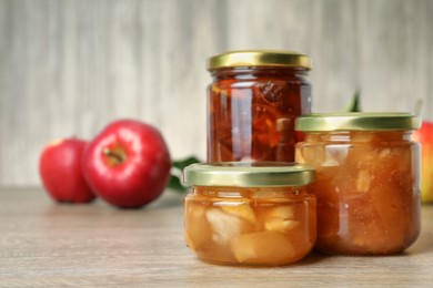 Photo of Tasty apple jam in glass jars on wooden table, space for text