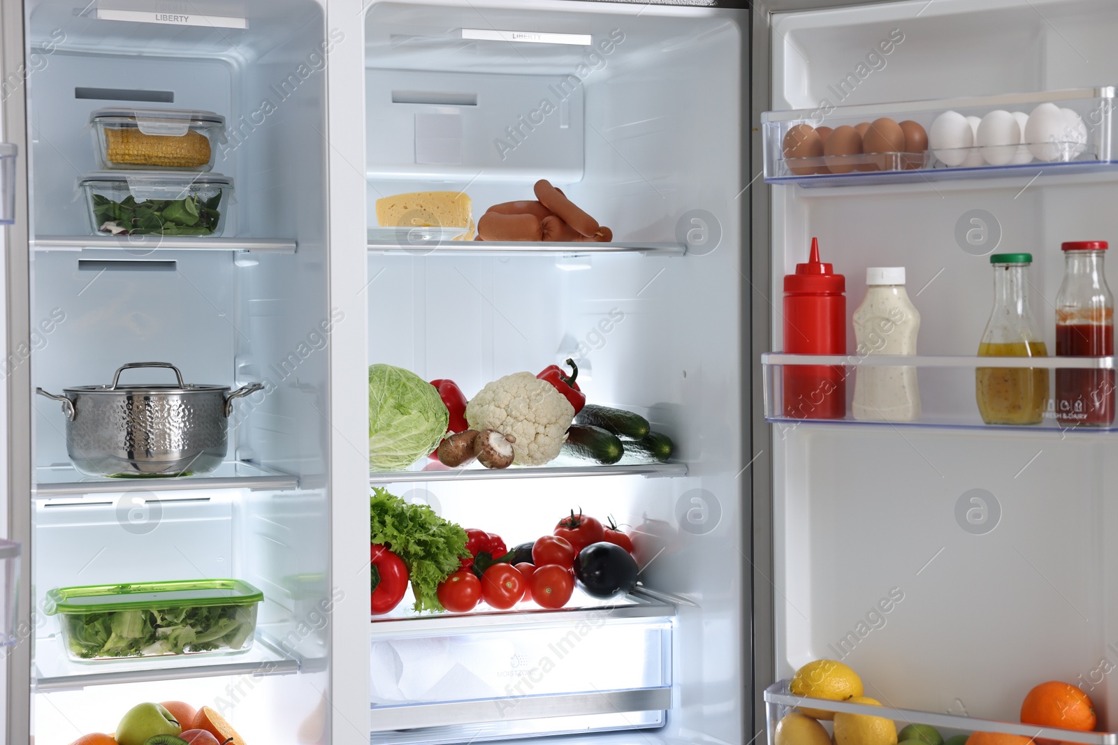 Photo of Open refrigerator full of different products indoors