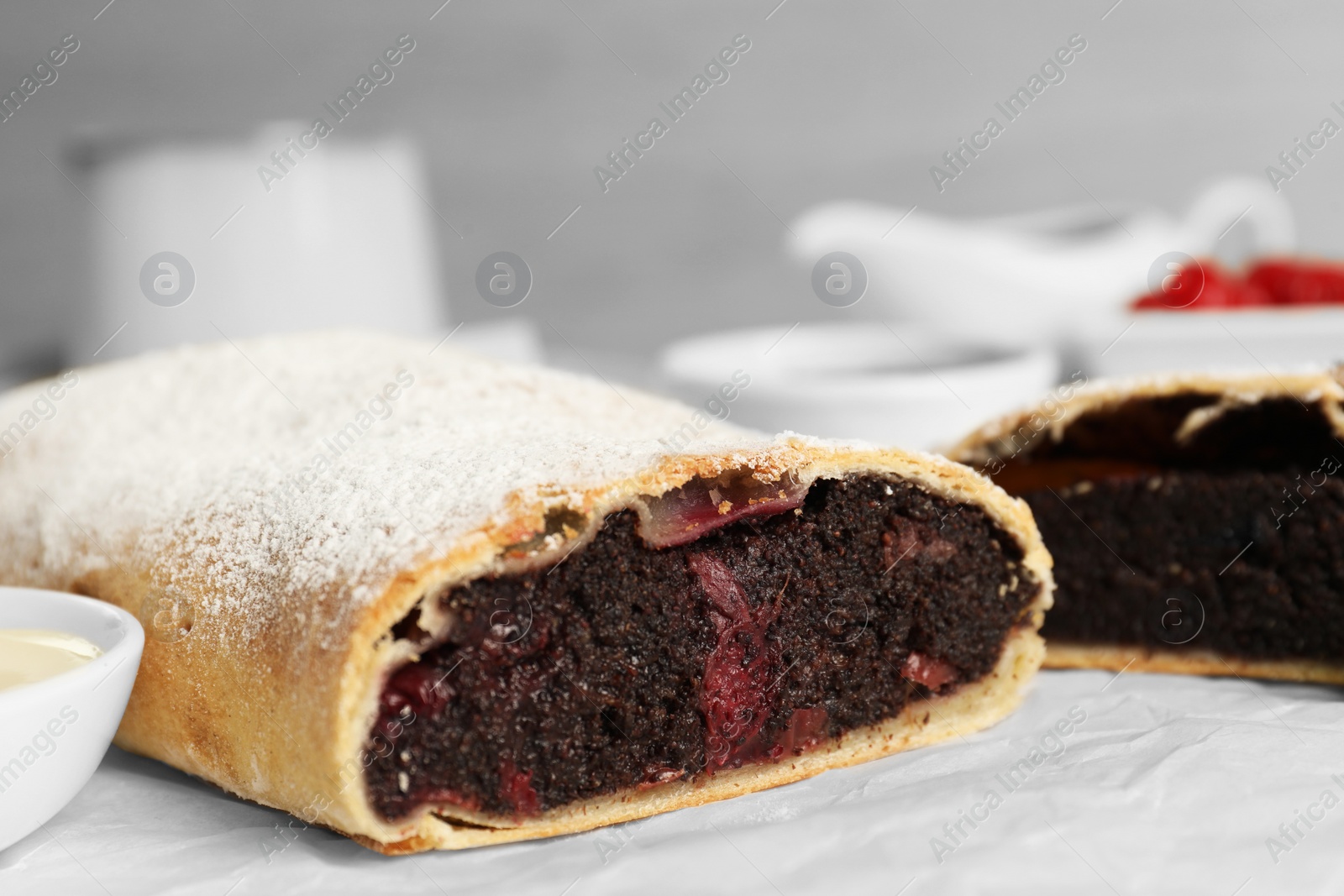 Photo of Delicious strudel with cherries and poppy seeds on parchment, closeup