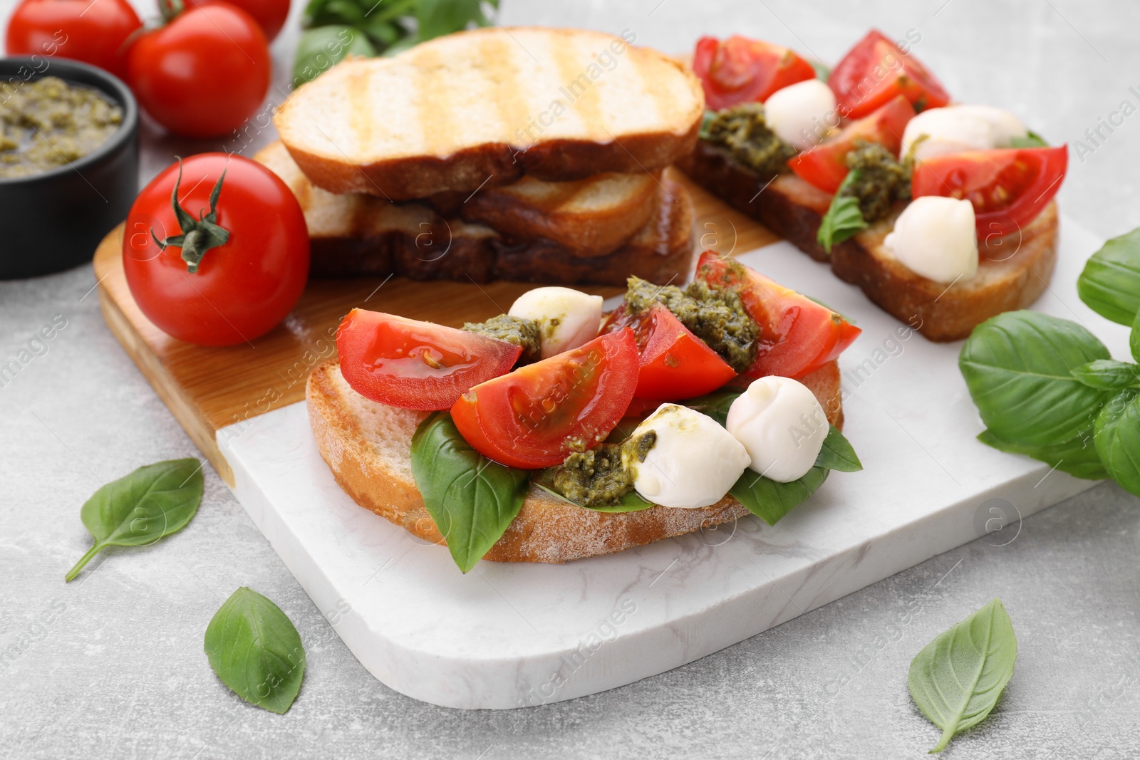 Photo of Delicious Caprese sandwiches with mozzarella, tomatoes, basil and pesto sauce on light grey table