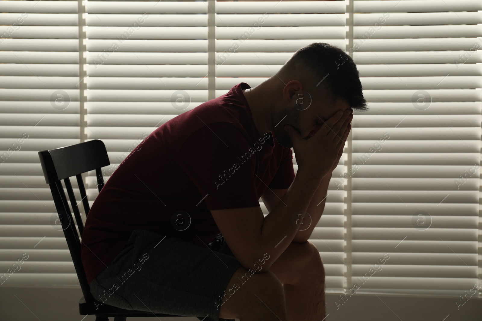 Photo of Sad man sitting near closed blinds indoors