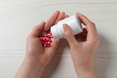 Photo of Woman pouring pills from bottle onto hand at white wooden table, top view
