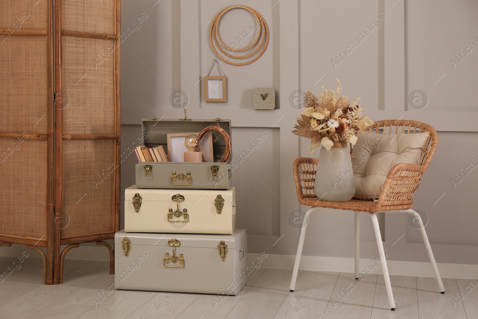 Photo of Wicker chair with dry flowers and storage trunks indoors. Interior design