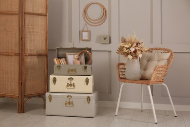 Photo of Wicker chair with dry flowers and storage trunks indoors. Interior design