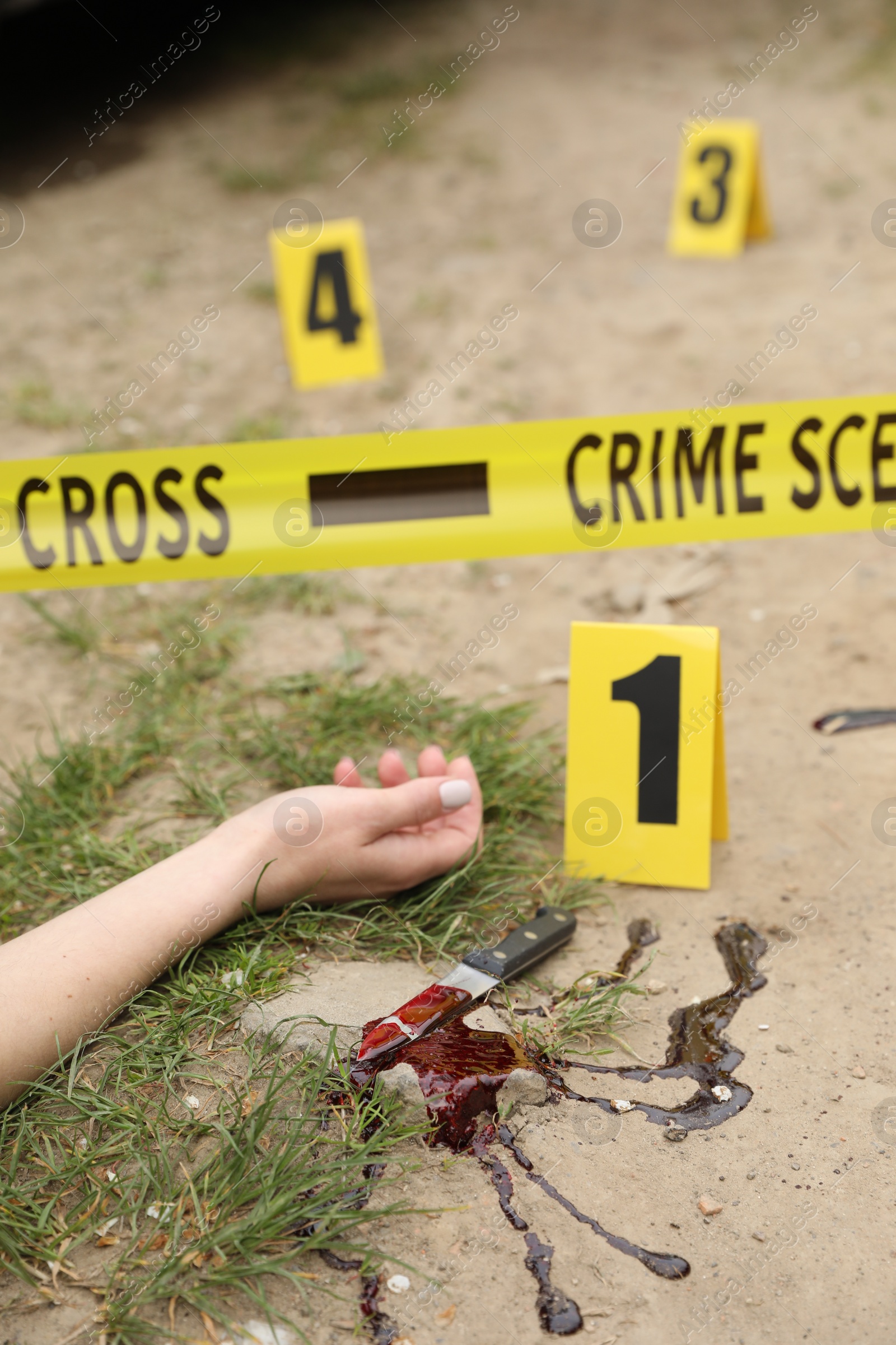 Photo of Crime scene with dead woman's body, markers, bloody knife and yellow tape outdoors, closeup