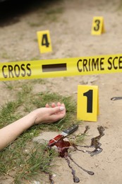 Crime scene with dead woman's body, markers, bloody knife and yellow tape outdoors, closeup