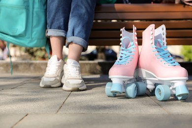 Photo of Woman with stylish pink roller skates sitting on bench outdoors, closeup