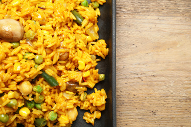 Photo of Delicious rice pilaf with vegetables on wooden table, top view. Space for text