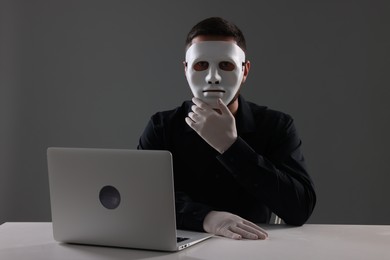 Photo of Man in mask and gloves sitting with laptop at white table against grey background
