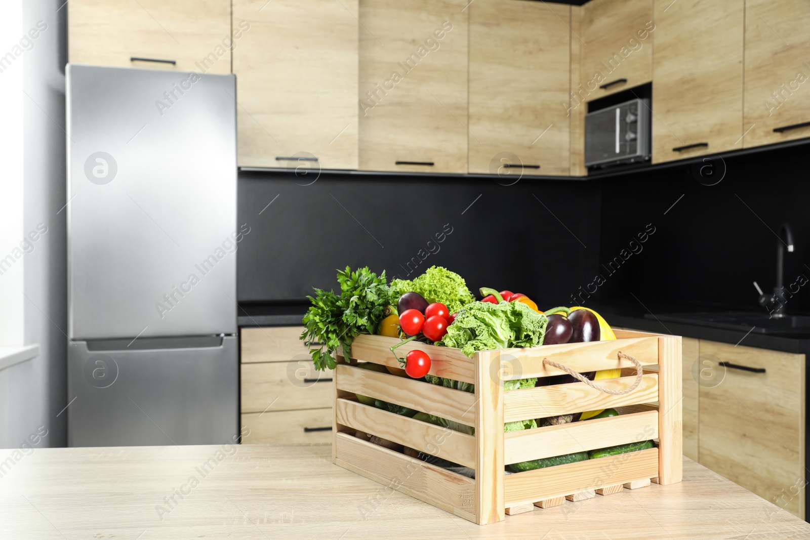 Photo of Wooden crate with vegetables on table in kitchen. Space for text