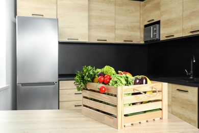 Photo of Wooden crate with vegetables on table in kitchen. Space for text