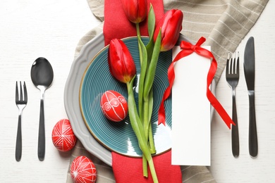 Festive Easter table setting with blank card and flowers on wooden background, top view. Space for text