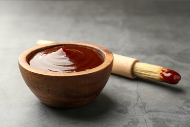 Photo of Tasty barbeque sauce in bowl and brush on grey textured table, closeup