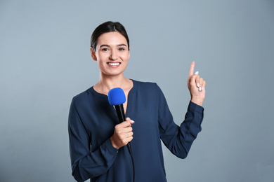 Photo of Young female journalist with microphone on grey background