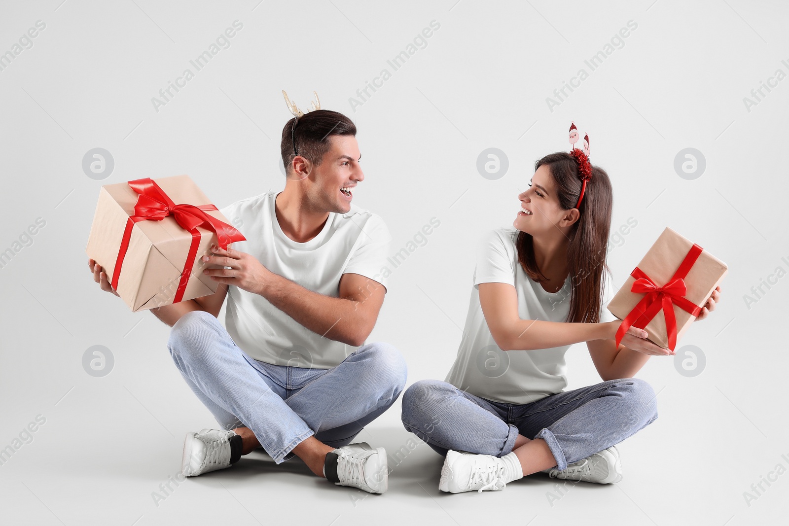 Photo of Beautiful happy couple in Christmas headbands  sitting with gifts on light background