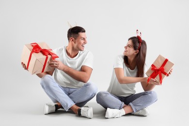 Beautiful happy couple in Christmas headbands  sitting with gifts on light background