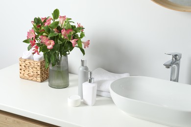 Photo of Vase with beautiful Alstroemeria flowers and toiletries near sink in bathroom