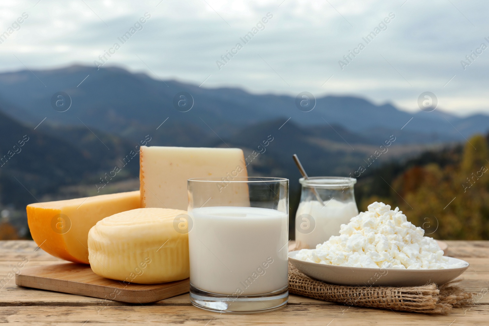 Photo of Tasty cottage cheese and other fresh dairy products on wooden table in mountains