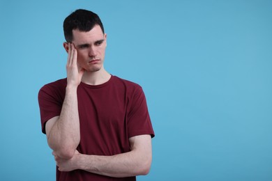 Portrait of sad man on light blue background, space for text