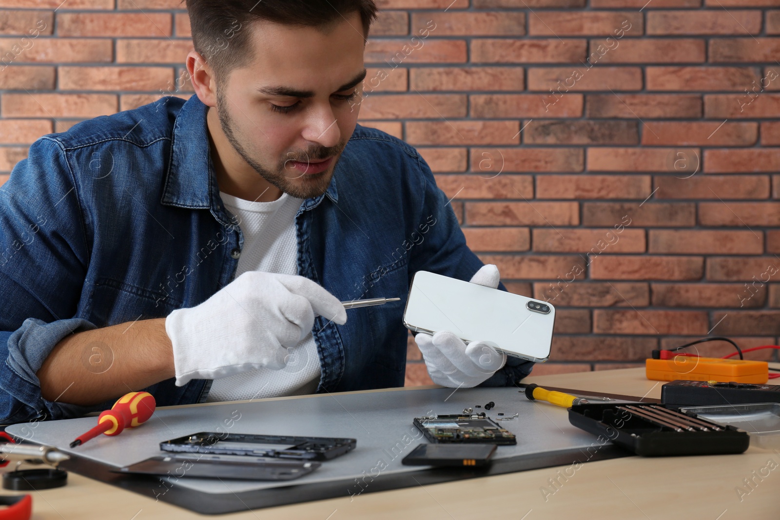 Photo of Technician repairing broken smartphone at table in workshop