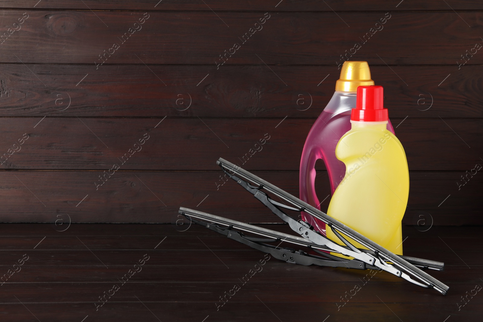 Photo of Bottles of windshield washer fluids and wipers on wooden table. Space for text