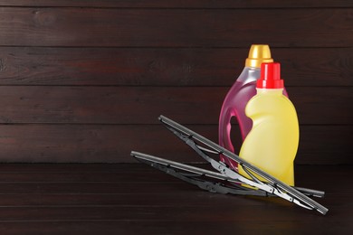 Photo of Bottles of windshield washer fluids and wipers on wooden table. Space for text