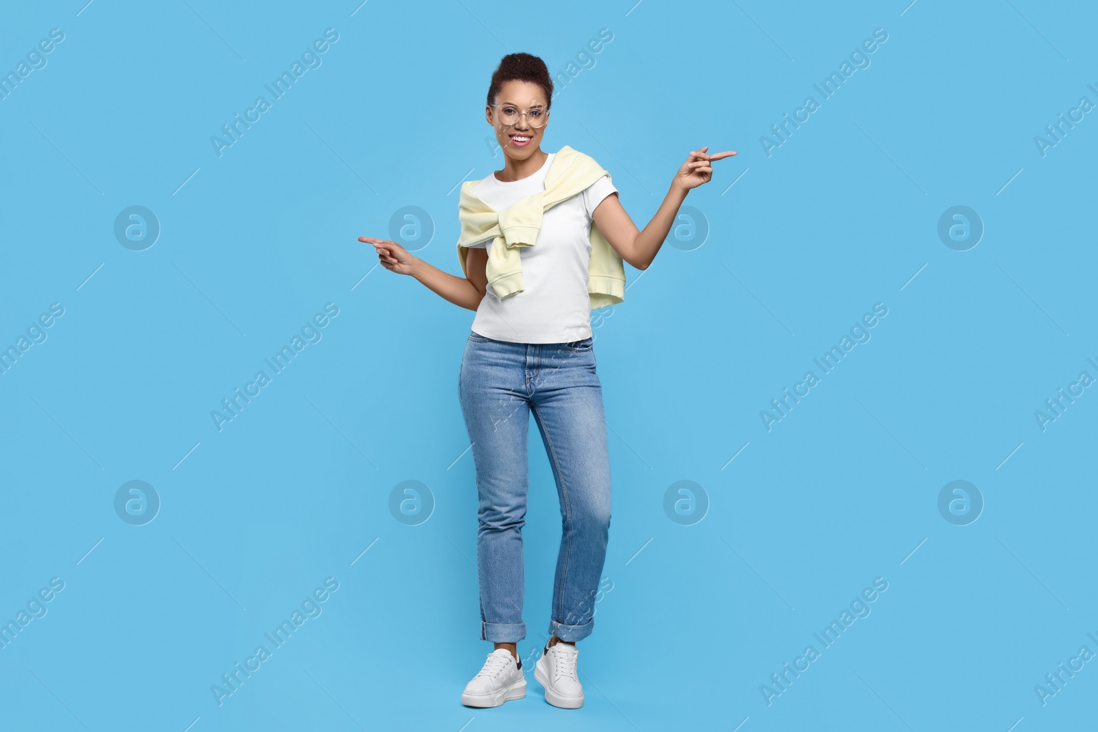 Photo of Happy young woman in stylish eyeglasses dancing on light blue background
